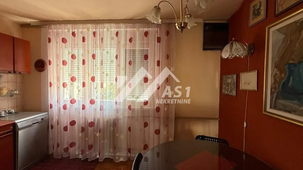 Trpezarija sa kuhinjom, stolom za ručavanje i prozorom sa zavesama.