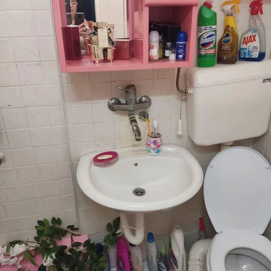 Manje kupatilo sa umivaonikom, WC šoljom i zidnim ormarićem.