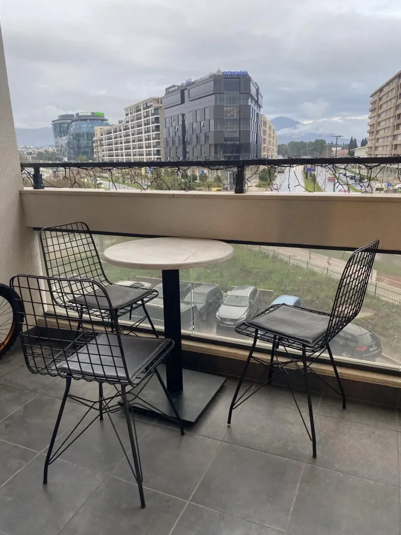 Balkon sa stolom, tri stolice i pogledom na grad.