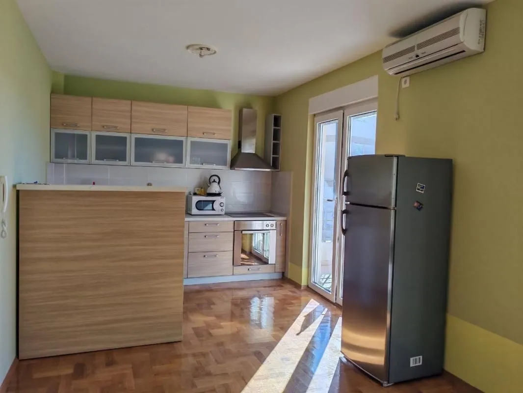 Kuhinja sa drvenim elementima, šankom i frižiderom.