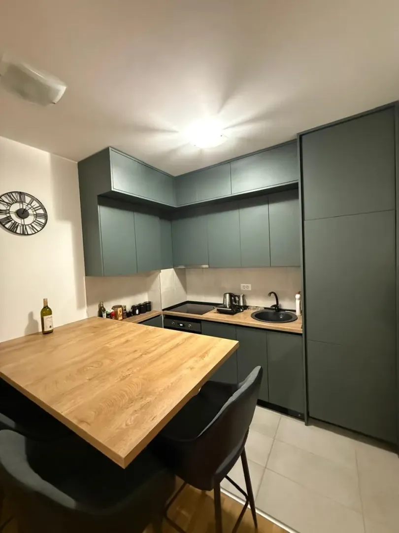 Modern kitchen with dark green cabinetry and a wooden dining table.