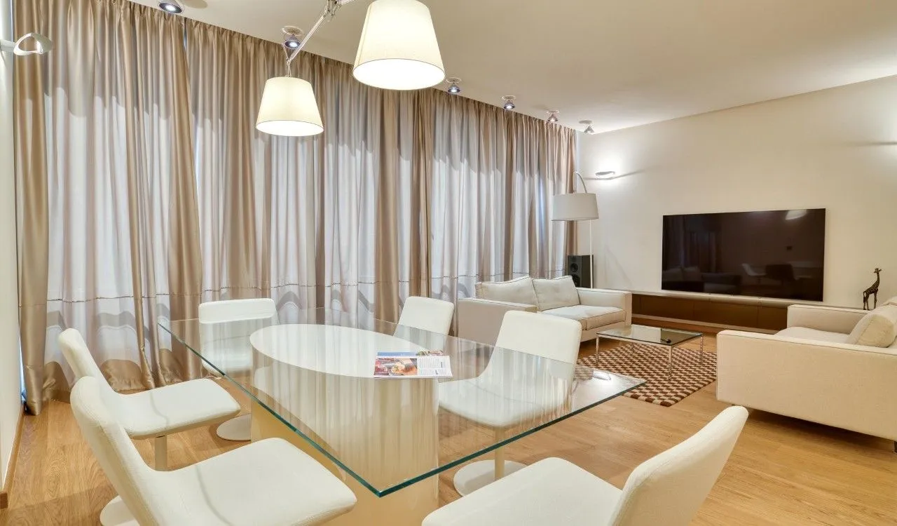 Spacious living room with a dining area, seating set, and large windows with curtains.