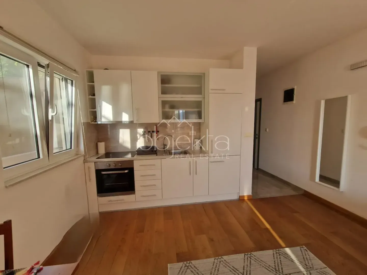 Small white kitchen with wooden flooring and a window.