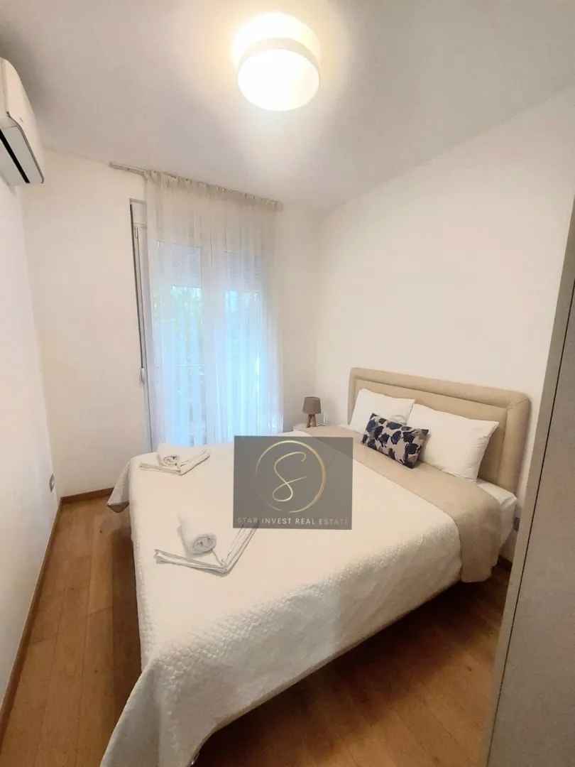 Furnished bedroom with a double bed and a window with white curtains.