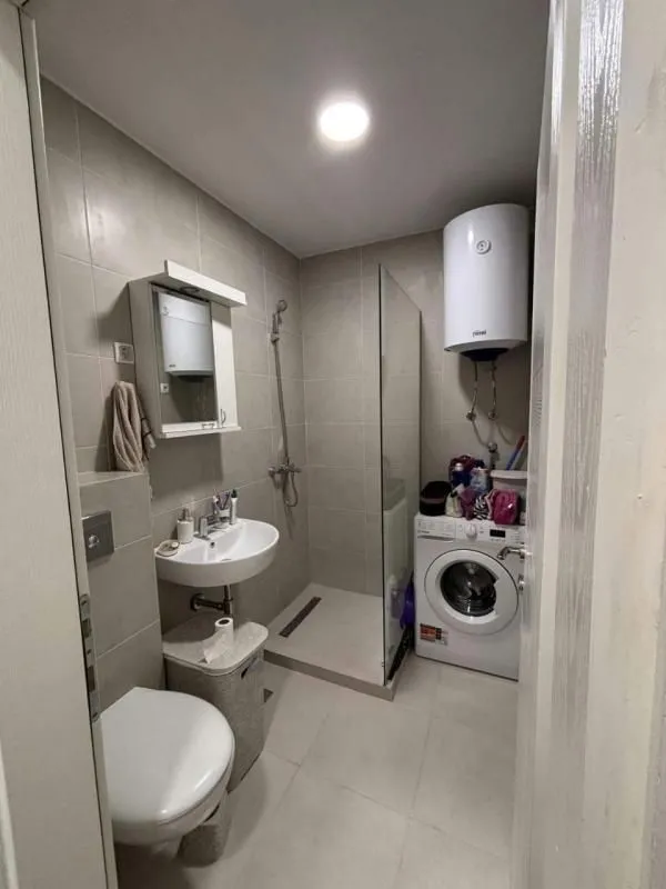 Manje kupatilo sa tuš kabinom, umivaonikom, WC šoljom i mašinom za veš.