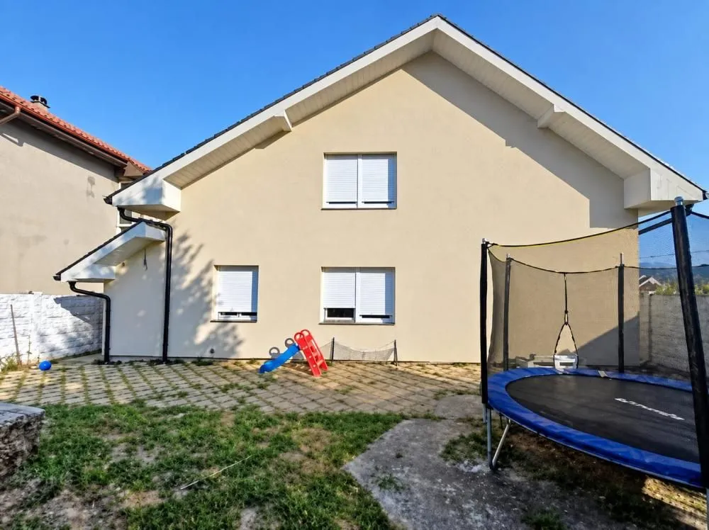 Zadnji deo kuće sa popločanim dvorištem, dečijim toboganom i trampolinom.