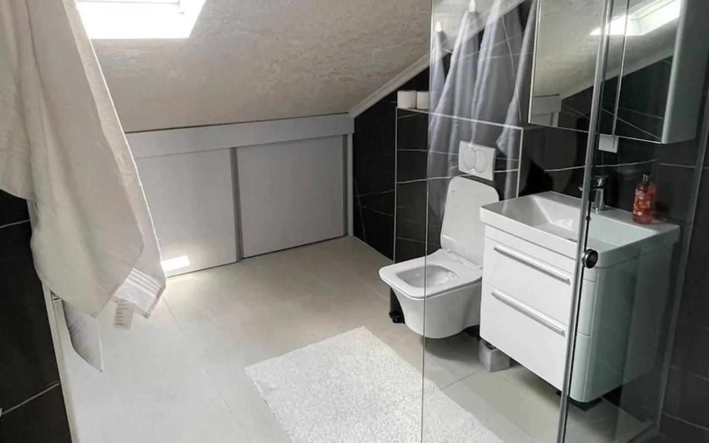 Modern attic bathroom equipped with a walk-in shower, toilet, and vanity unit.