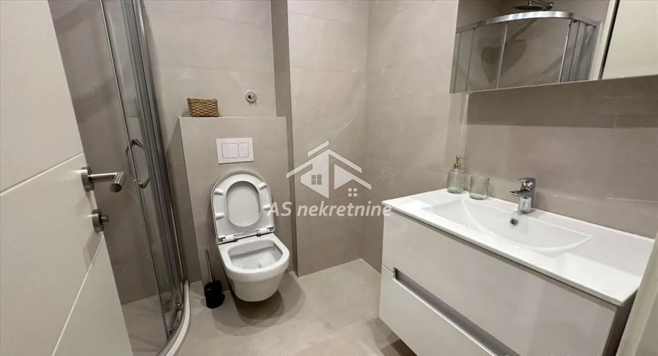 Moderno kupatilo sa tuš kabinom, umivaonikom i WC šoljom.