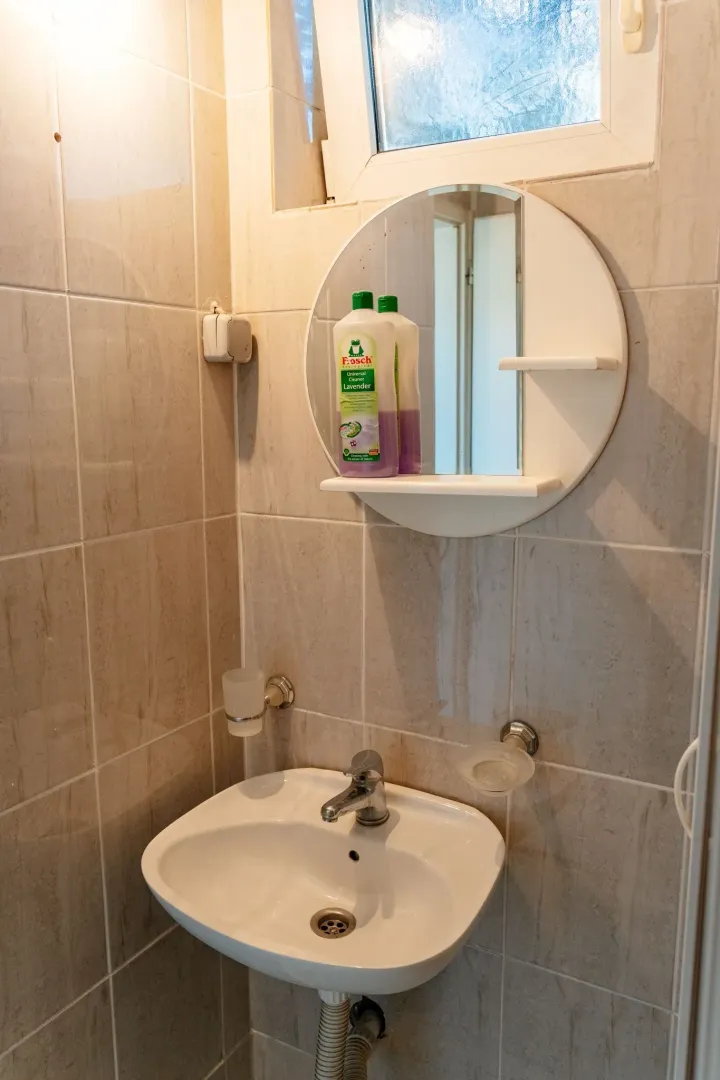 A simple sink with a mirror in a bathroom with light tiles.