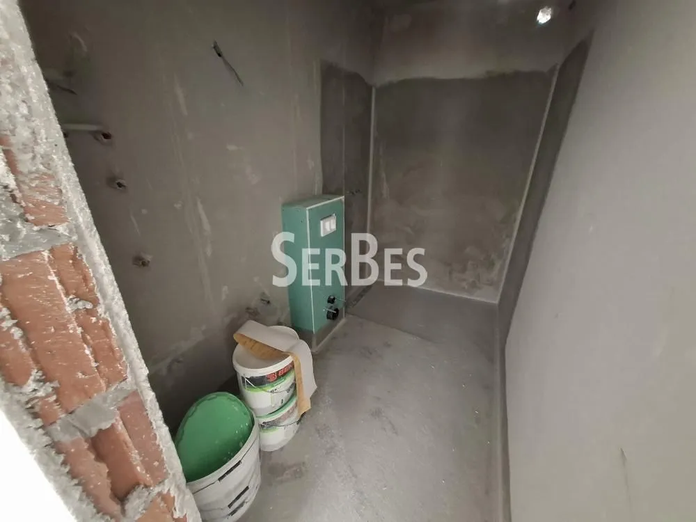 Pogled na nenamestenu prostoriju u izgradnji sa betonskim zidovima i građevinskim materijalom.