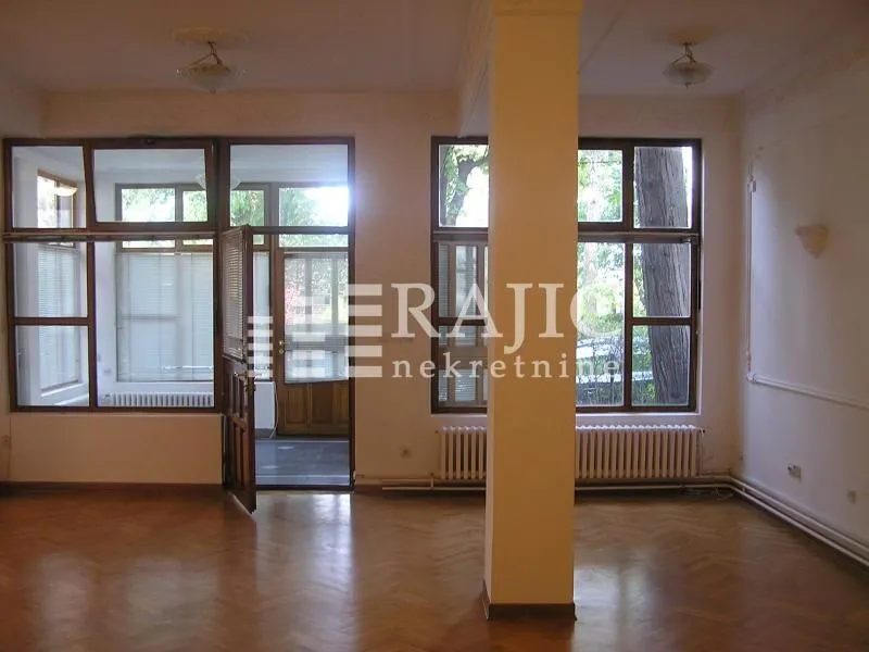Empty living room with parquet flooring and large windows.