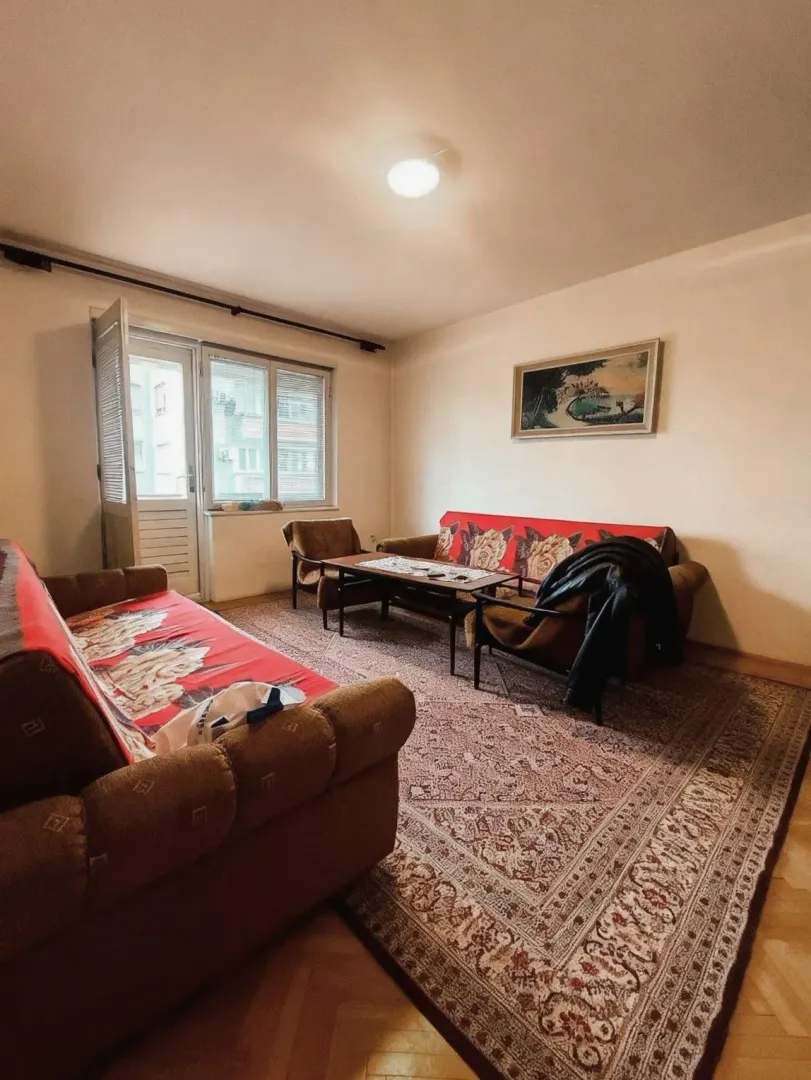 Dnevna soba sa garniturom, tepihom i izlazom na terasu.
