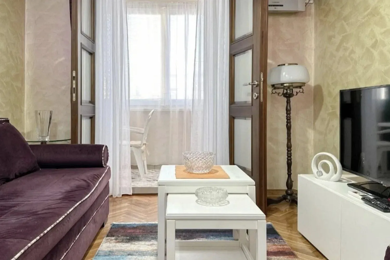Dnevna soba sa garniturom, stočićem, televizorom i izlazom na terasu.