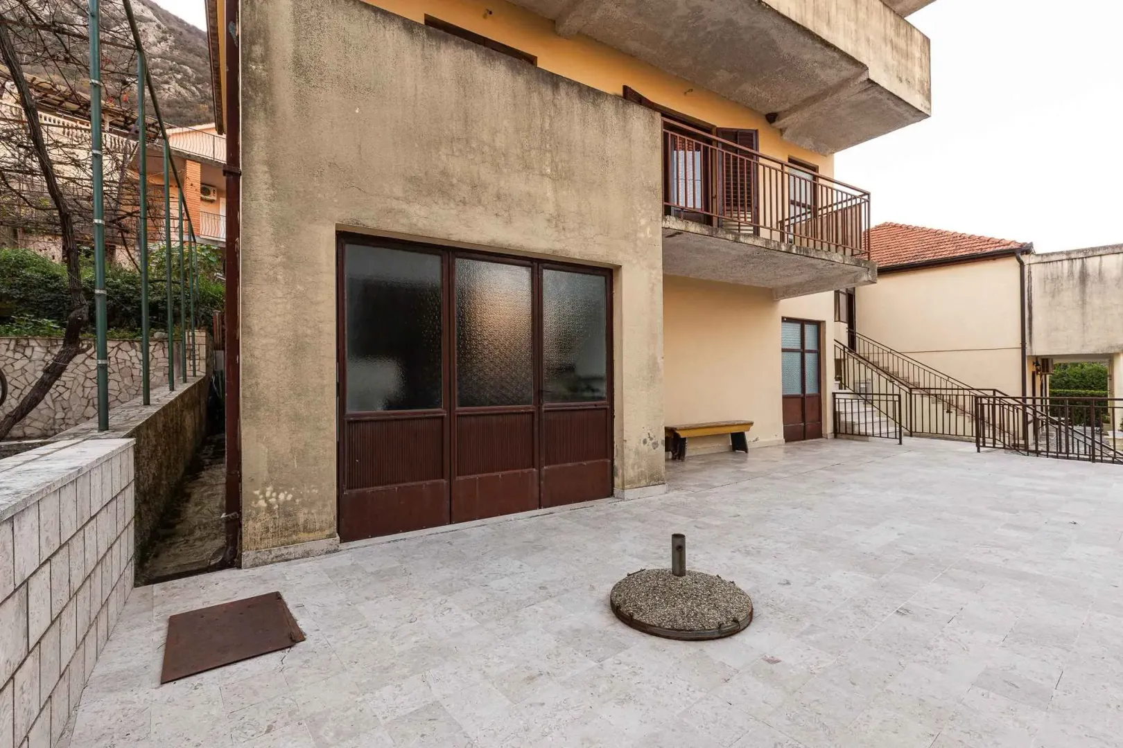 Pogled na dvorište i fasadu kuće sa balkonom i stepeništem.