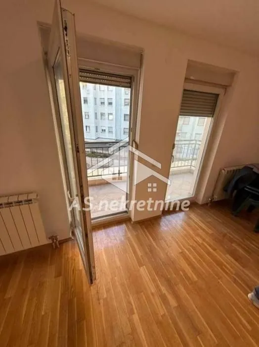 Prazna soba sa drvenim podom i izlazom na balkon.