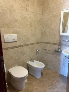 Kupatilo opremljeno WC šoljom, bideom, umivaonikom i zidnim pločicama u bež tonovima. - image 8