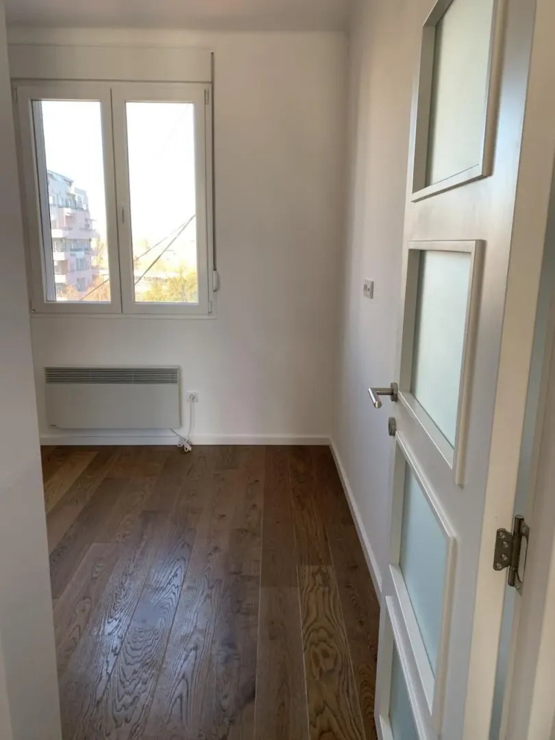 Empty bright room with wooden flooring, a window, and a door with glass panels.
