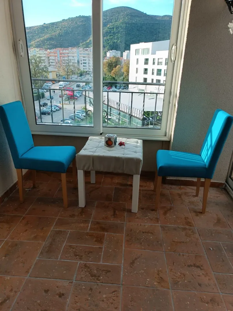 Covered terrace with two blue chairs and a small table with a city view.