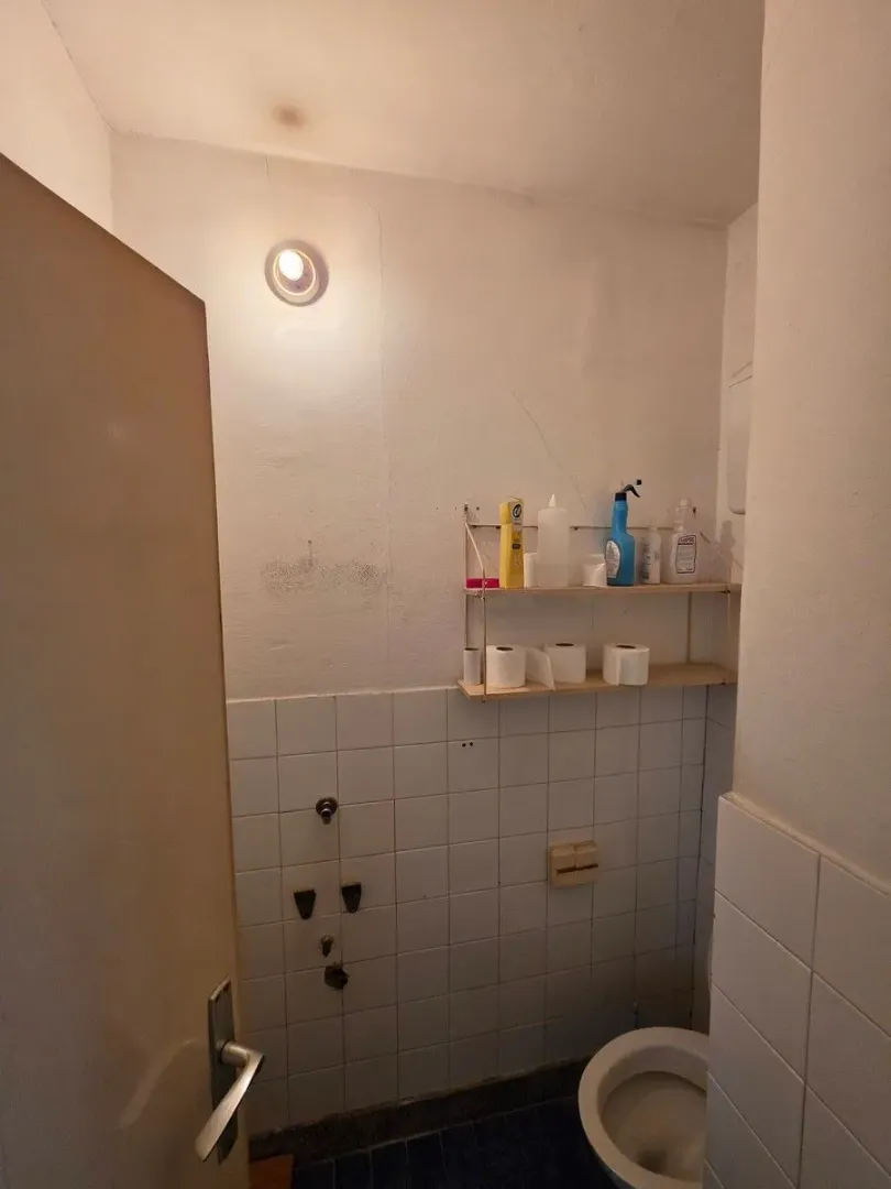 Manje kupatilo sa toaletom i policom za odlaganje potrepština.