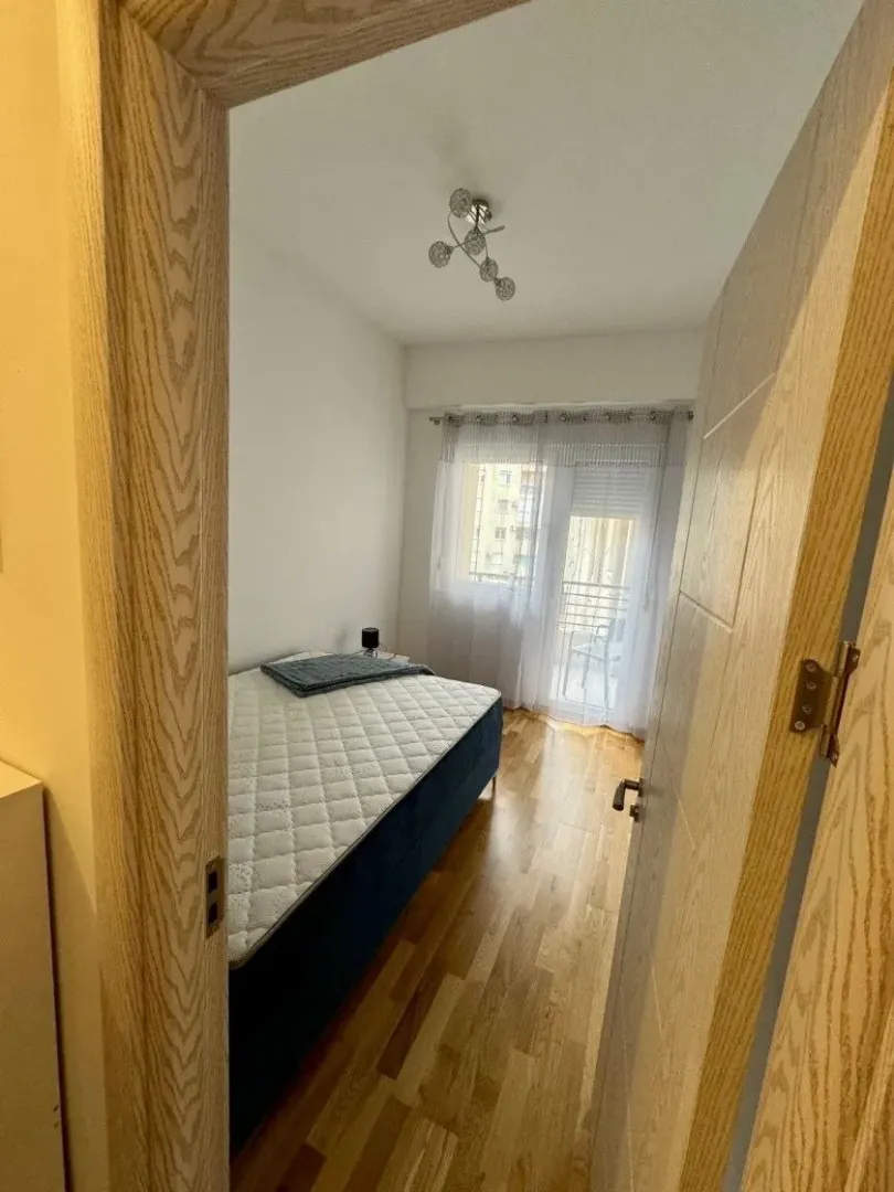 Pogled iz hodnika na manju spavaću sobu sa krevetom i izlazom na terasu.