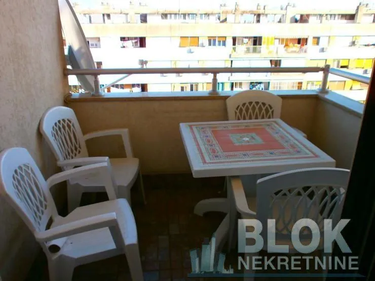 Small furnished balcony with a table and plastic chairs.