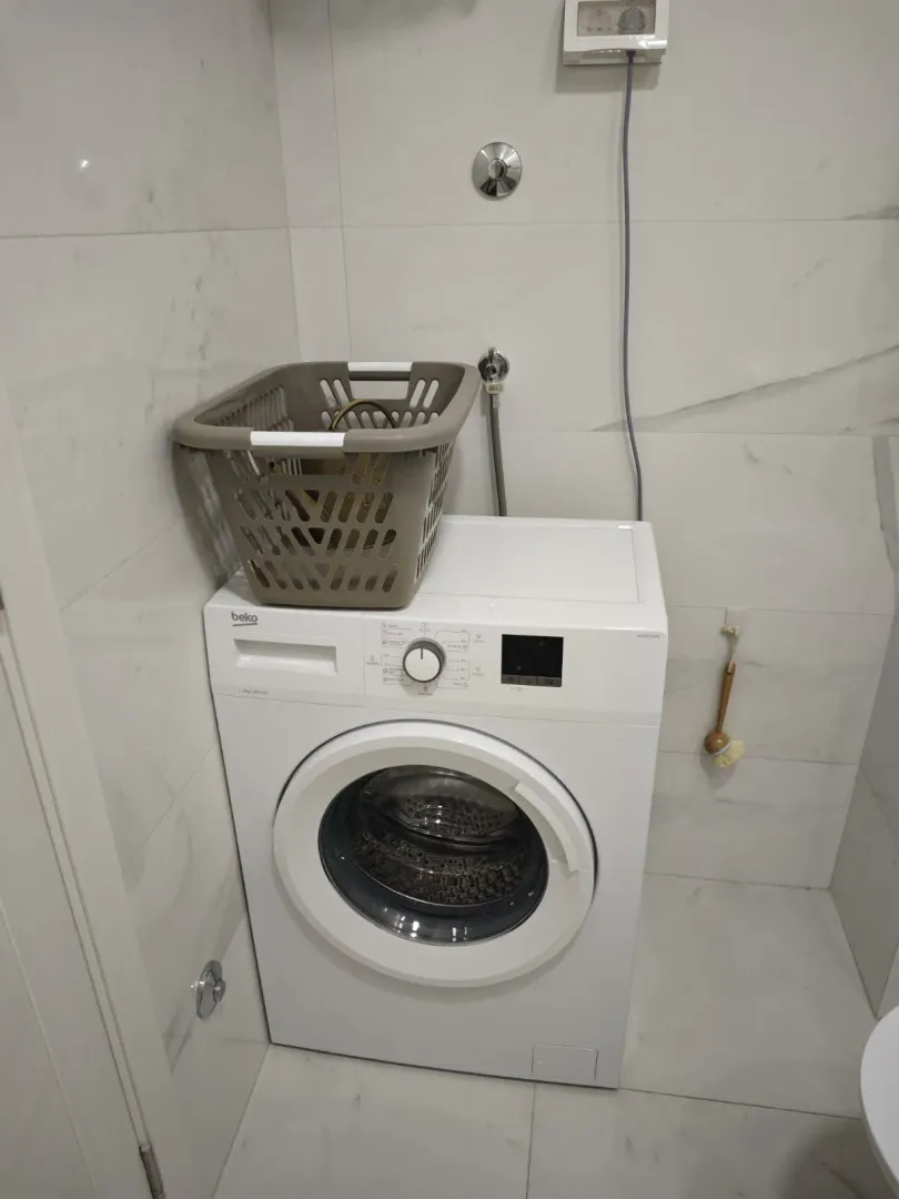 Veš mašina u kupatilu sa bijelim pločicama.