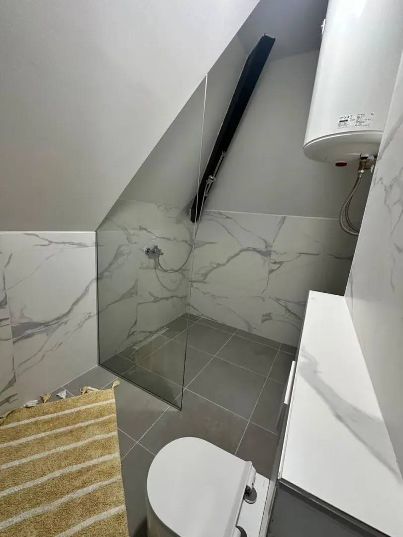 Moderno opremljeno kupatilo sa tuš kabinom pod kosinom krova.