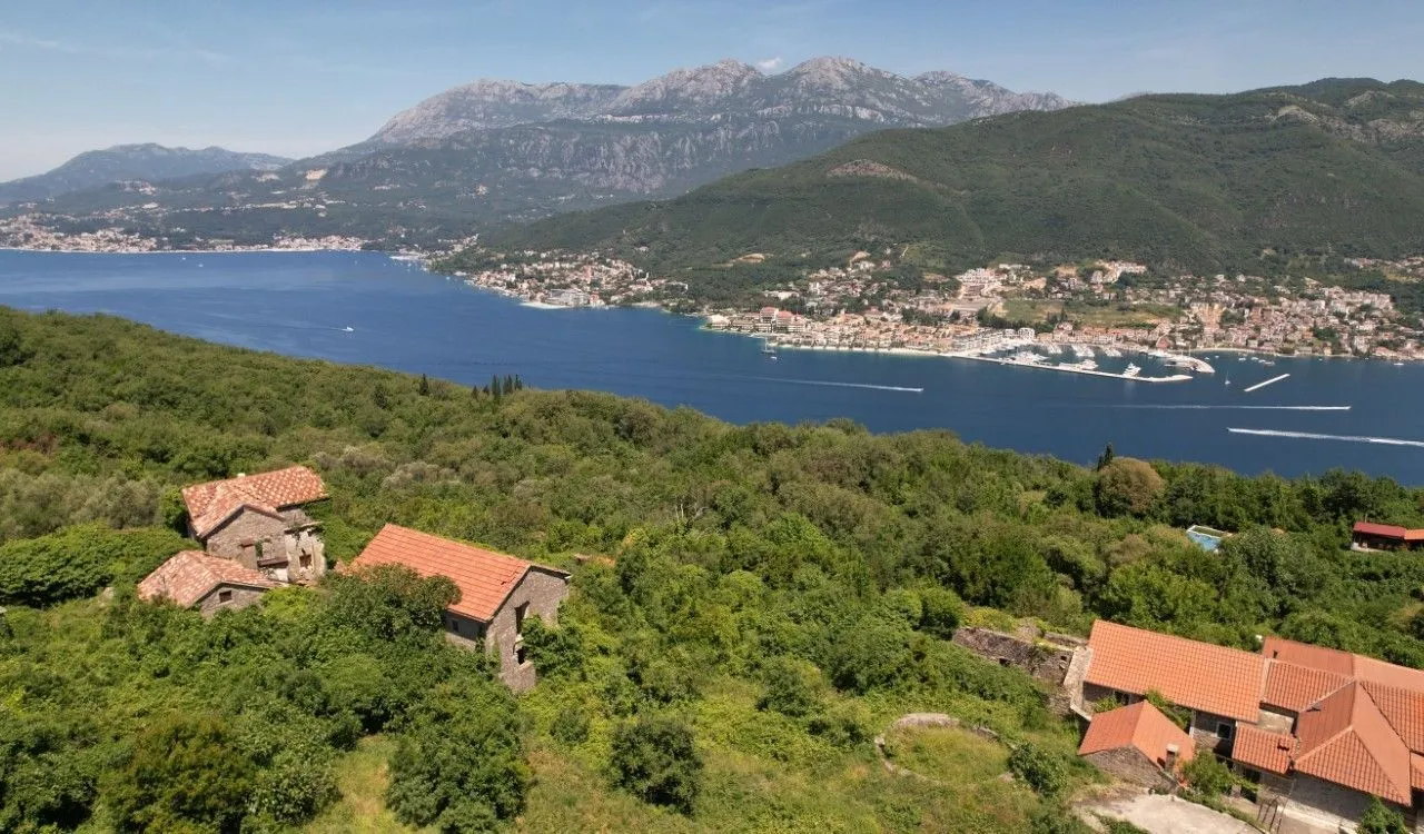 Pogled iz vazduha na stare kamene kuće okružene zelenilom sa pogledom na more.