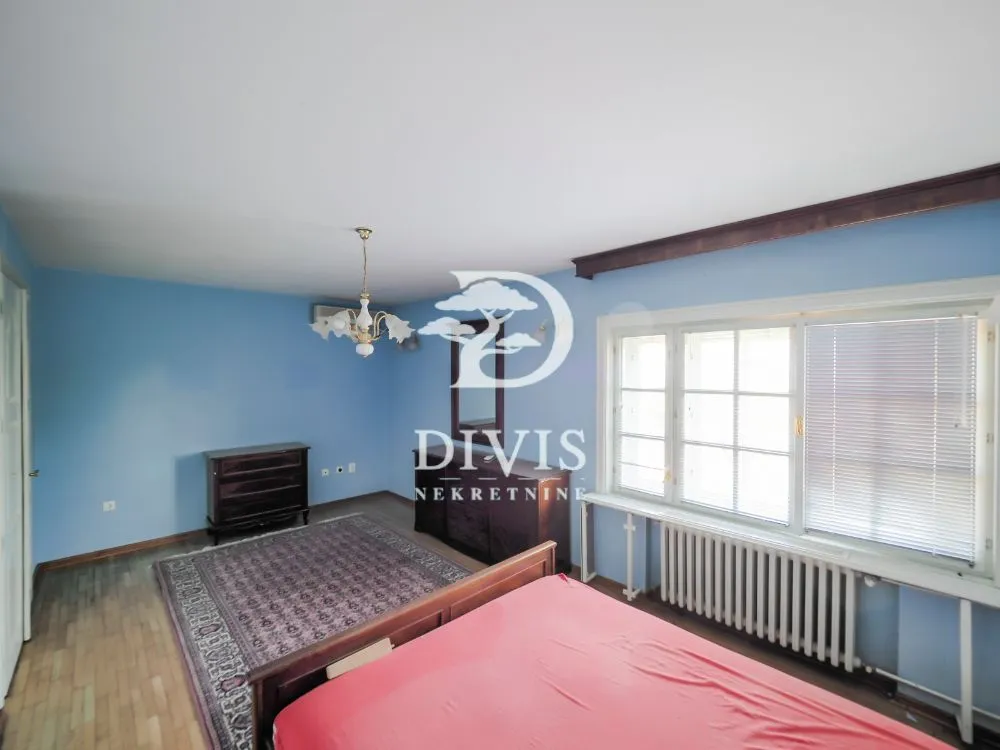 Spacious bedroom with a bed, blue walls, and a large window.