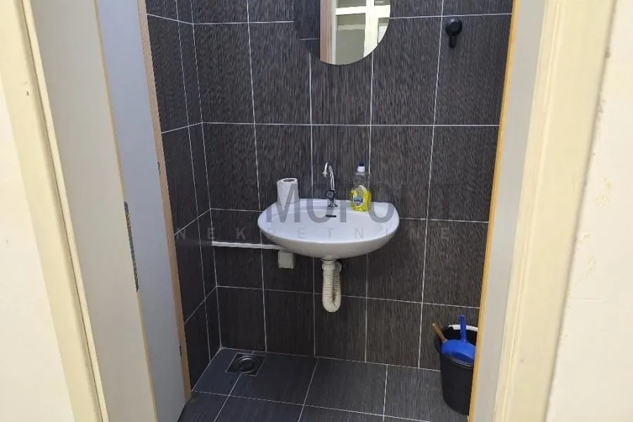 Smaller bathroom lined with dark tiles featuring a washbasin and a mirror.