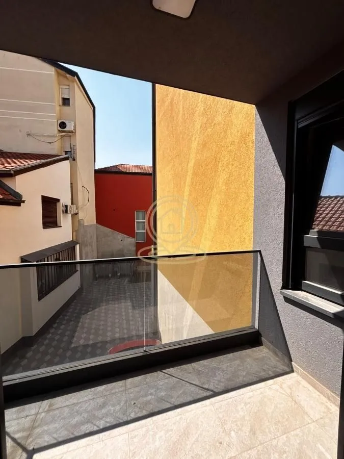 Small covered balcony with a glass railing and a view of neighboring buildings.
