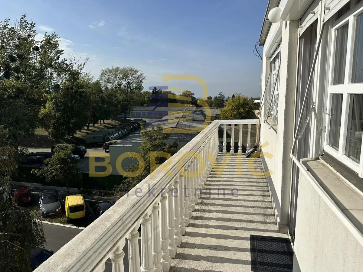 Dugačak balkon sa belom ogradom i pogledom na okolinu.