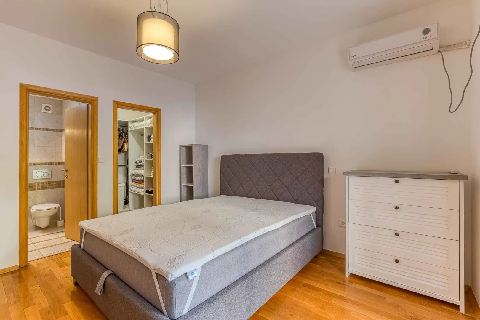 Bedroom with a double bed, dresser, air conditioner, and views into the bathroom and walk-in closet.