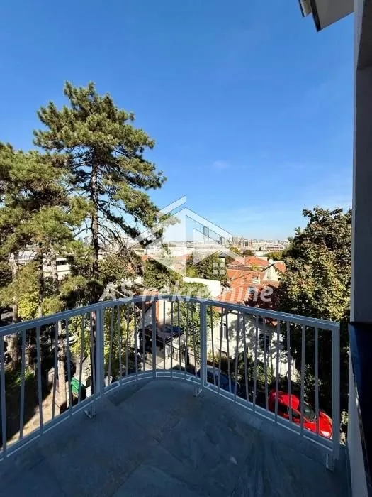 Pogled sa balkona na okolne zgrade i drveće.