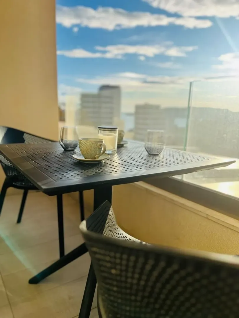 Namješten balkon sa stolom, stolicama i pogledom na grad i more.