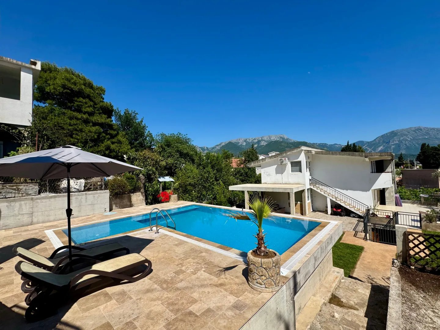 View of the outdoor swimming pool with sun loungers and an umbrella in the yard of the house.