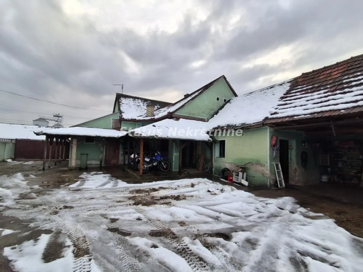 Pogled na dvorište i spoljašnjost kuće sa snegom pokrivenim krovom.