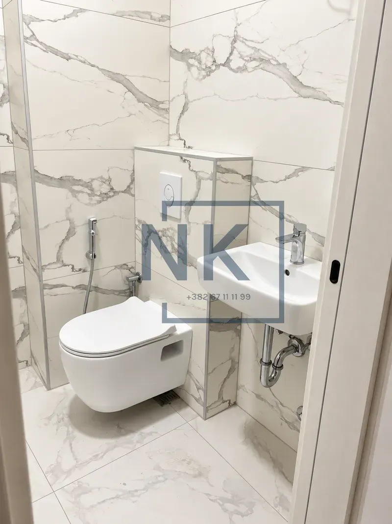 Small bathroom featuring white marble-effect ceramic tiles, a wall-hung toilet, and a sink.