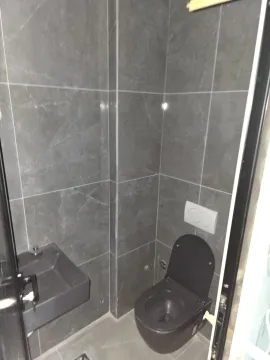 Small toilet room with grey tiles, a dark toilet, and a small sink. - image 7
