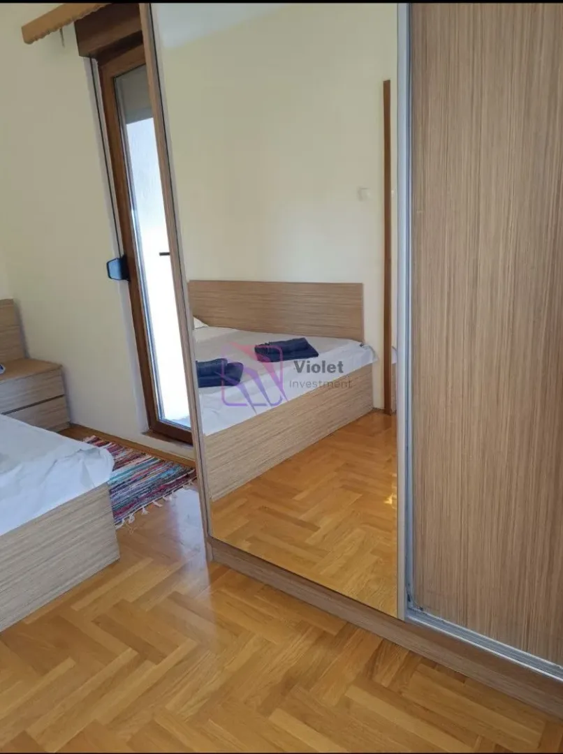 Spavaća soba sa drvenim krevetom, parketom i velikim ormarom sa ogledalom.