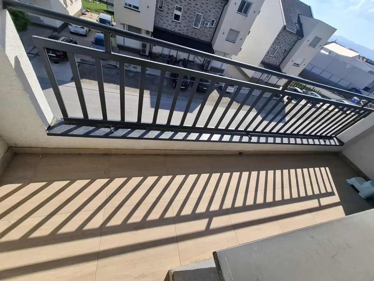 Balkon sa metalnom ogradom i pogledom na naselje i parking.