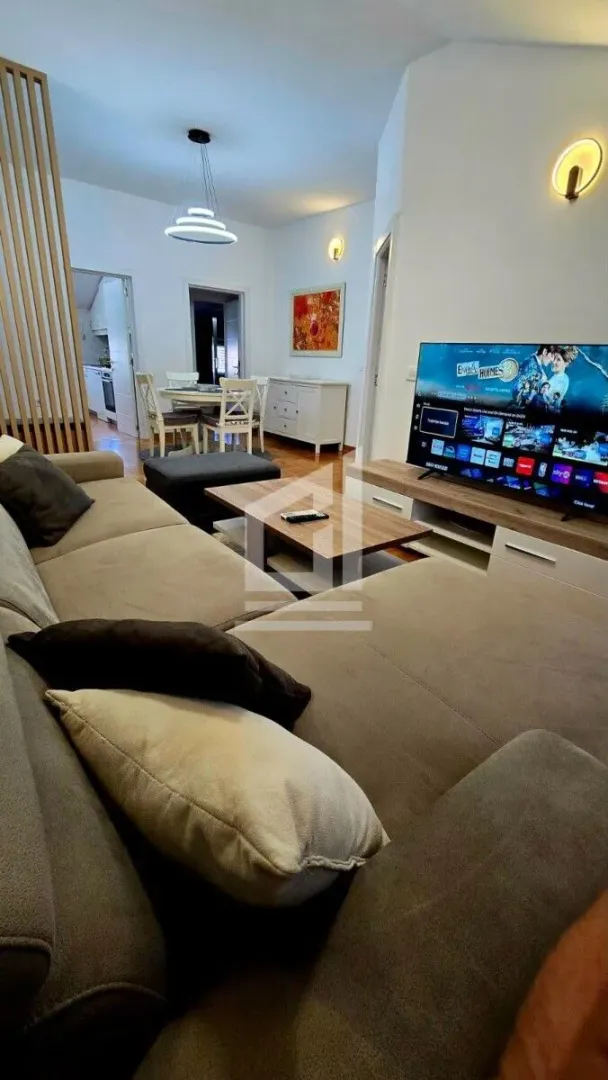 Living room with a sofa, TV, and a dining area in the background.