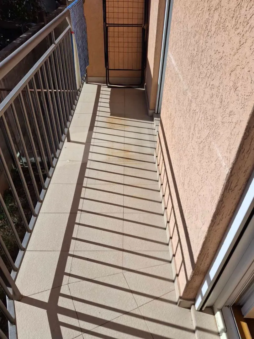 Uski balkon sa pločicama i metalnom ogradom.