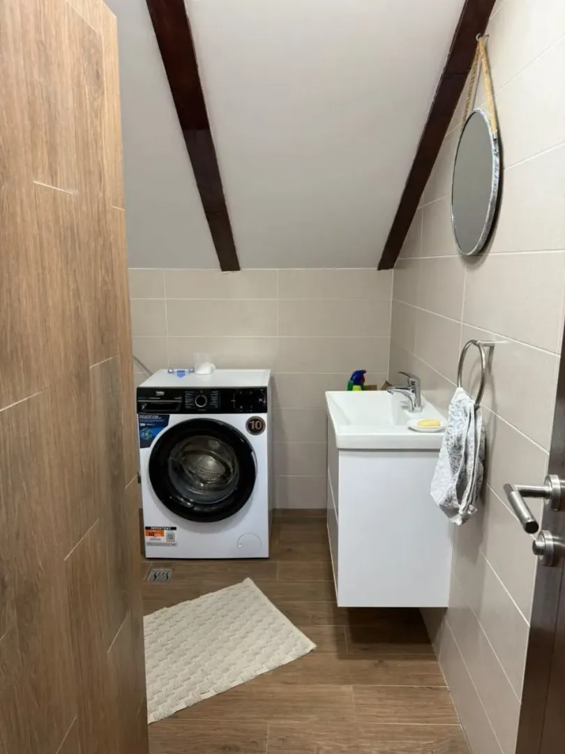 Compact bathroom with a sink and washing machine under a sloped ceiling.
