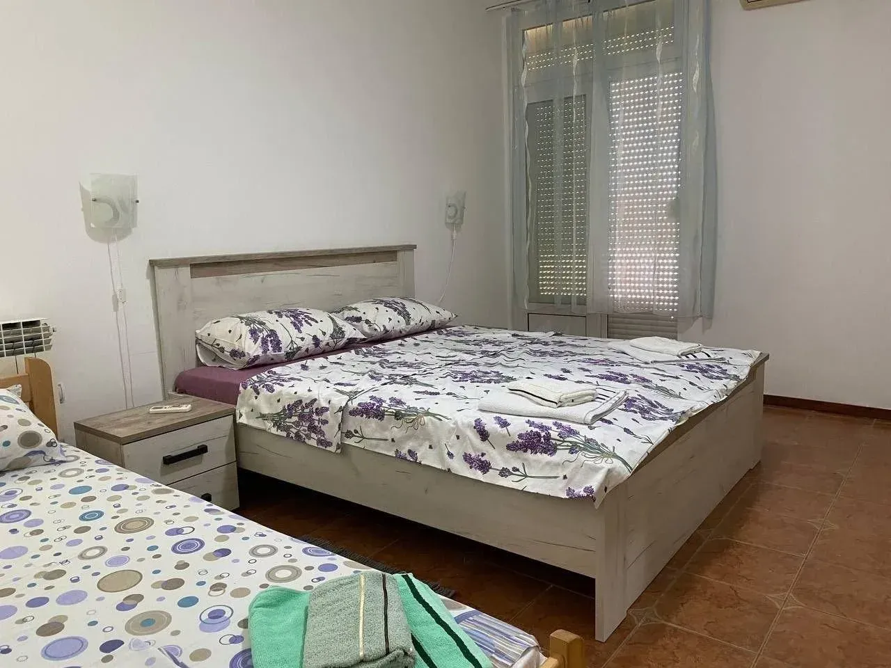 Spavaća soba sa bračnim krevetom, noćnim stočićem i prozorom.