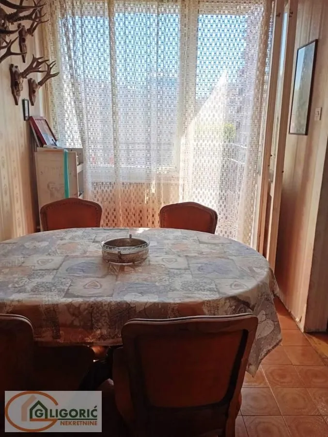 Trpezarija sa okruglim stolom i stolicama blizu prozora sa zavesama.