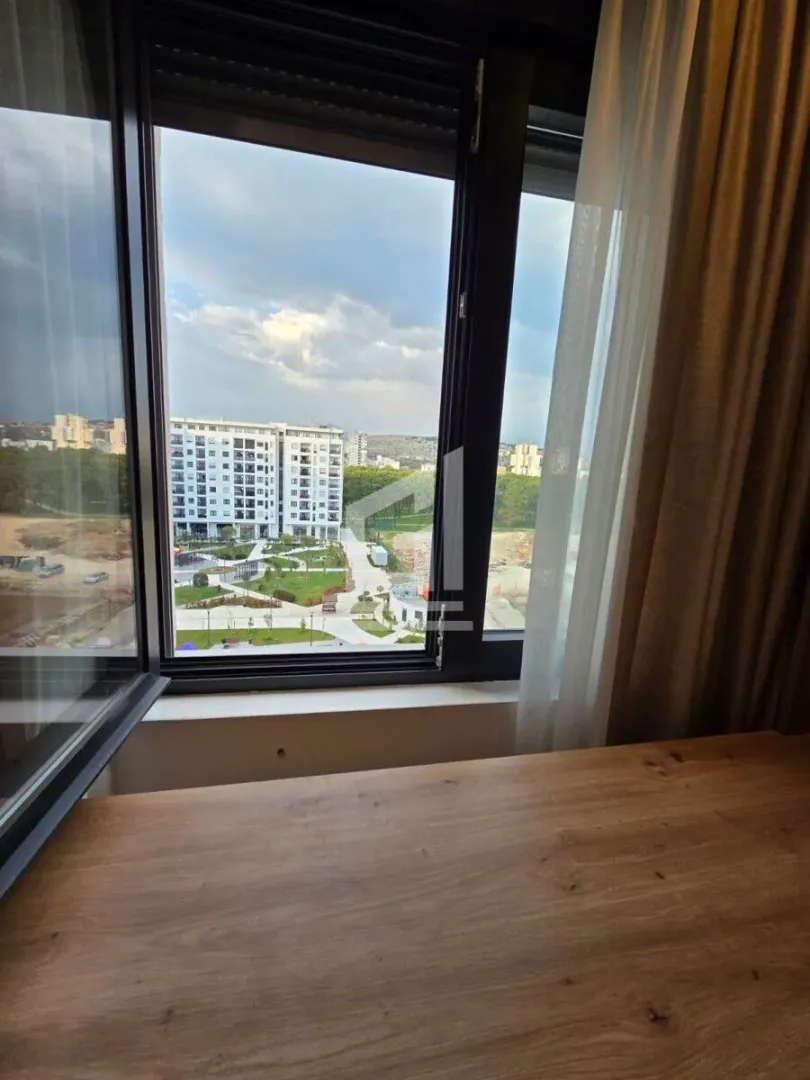 Pogled kroz prozor na okolne zgrade i zelene površine.