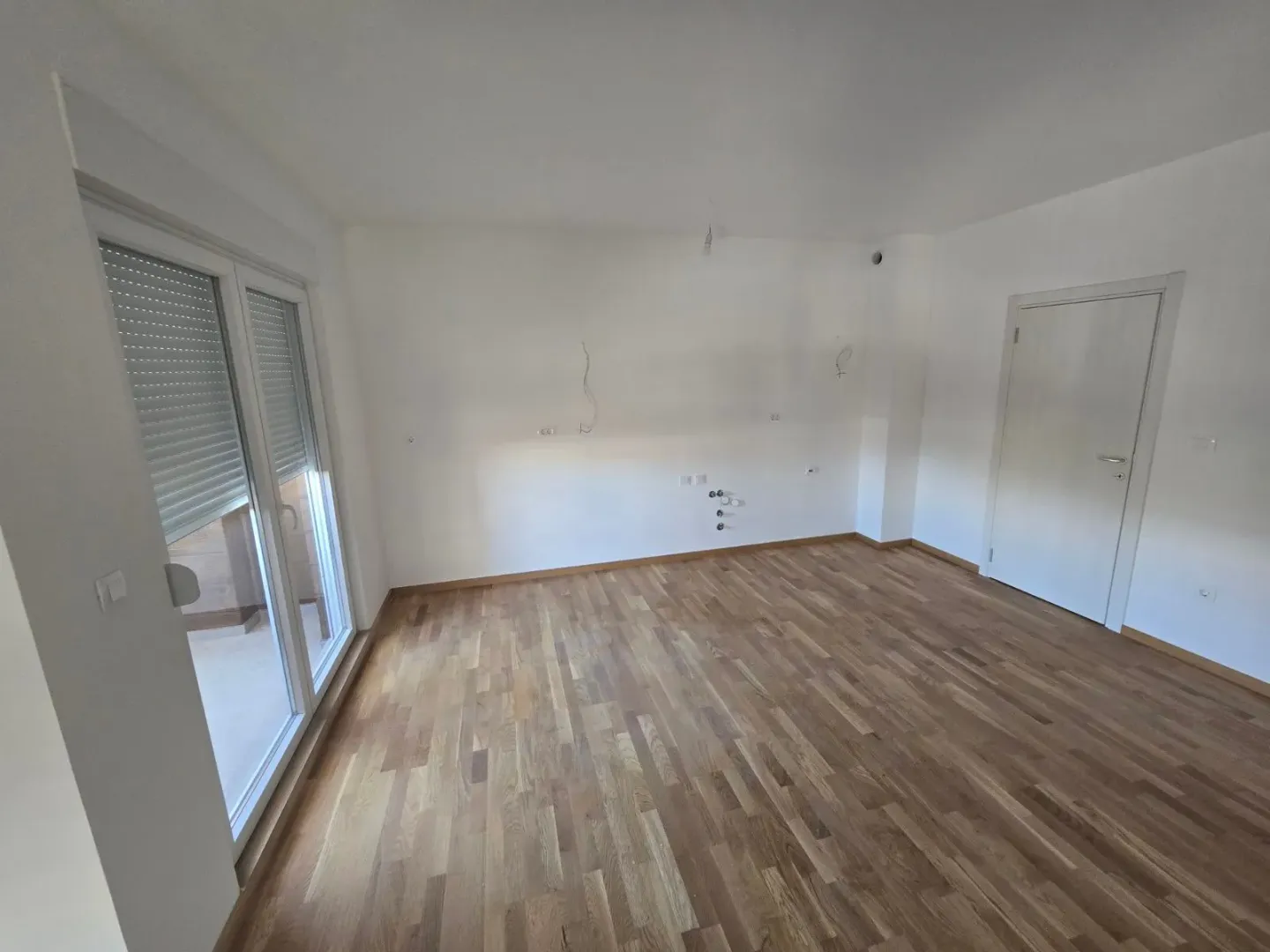 Prazna soba sa parketom i balkonskim vratima.