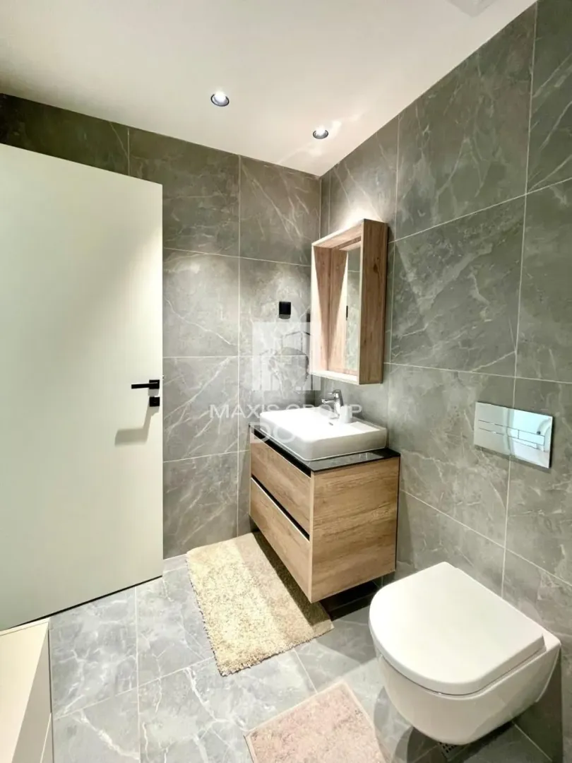 Modern bathroom with grey tiles, vanity sink, and wall-mounted toilet.