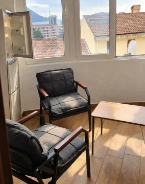 Dnevna soba sa foteljama, stočićem i frižiderom kraj prozora sa pogledom na grad. - image 5